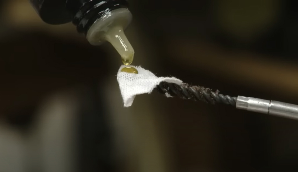 A drop of gun oil being applied to a cleaning patch on a gun cleaning rod